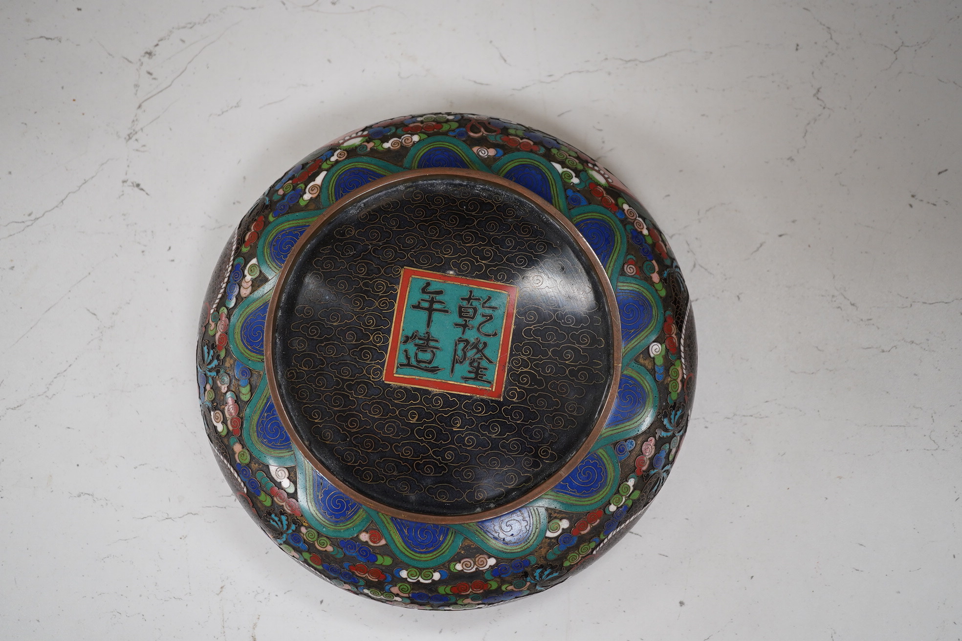 A Chinese cloisonné enamel ‘dragon’ bowl, Qianlong mark but early 20th century, on hardwood stand, 20cm diameter. Condition - poor to fair